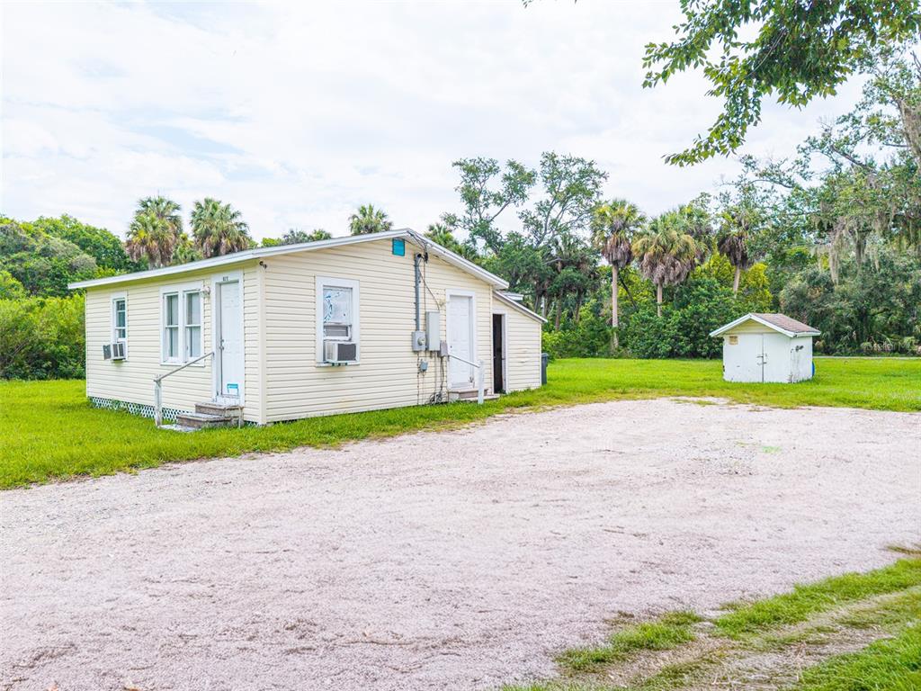 A light yellow house with a gravel driveway and a small shed in the yard — 6315 RHONDA ROAD, TAMPA, FL