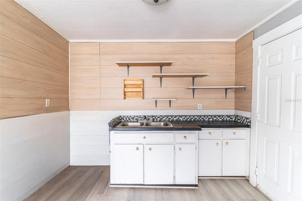 A kitchen area features white cabinets, a double sink, open shelving, and wood-paneled walls — 6315 RHONDA ROAD, TAMPA, FL
