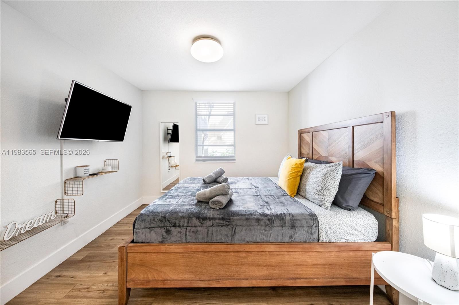 A bedroom features a wooden bed frame, a wall-mounted television, and light wood flooring — 237 38th St # 4, Miami Beach FL 33140, MIAMI BEACH, FL