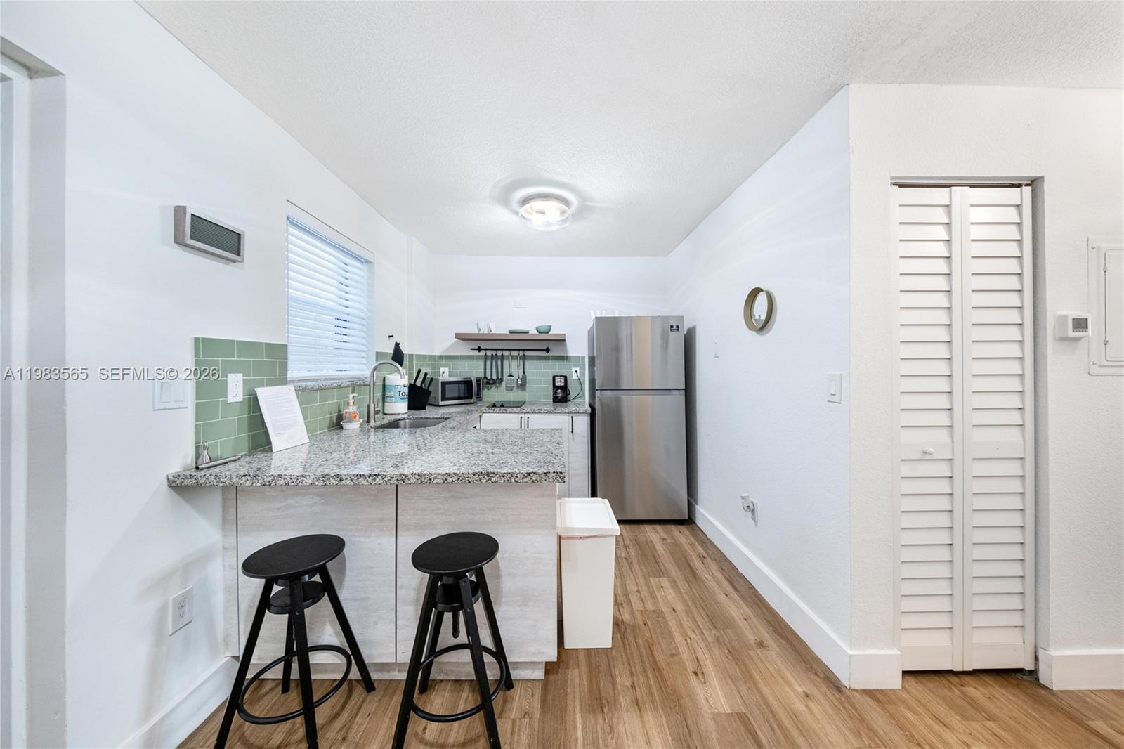 A small kitchen features granite countertops, a stainless steel refrigerator, and two black bar stools — 237 38th St # 4, Miami Beach FL 33140, MIAMI BEACH, FL