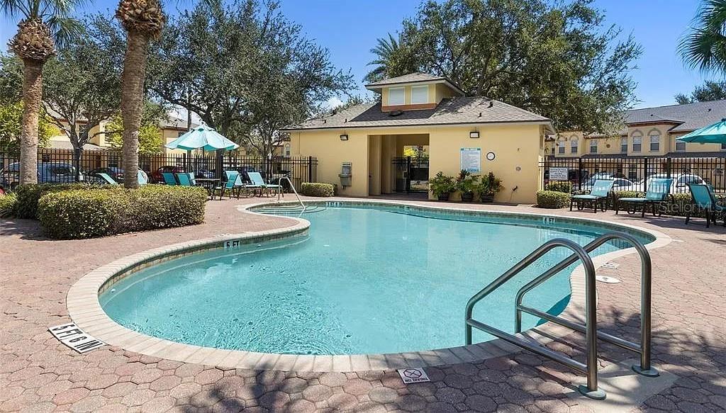 A swimming pool with a metal ladder sits in front of a community clubhouse building — 3874 MARINER DRIVE, ST PETERSBURG, FL