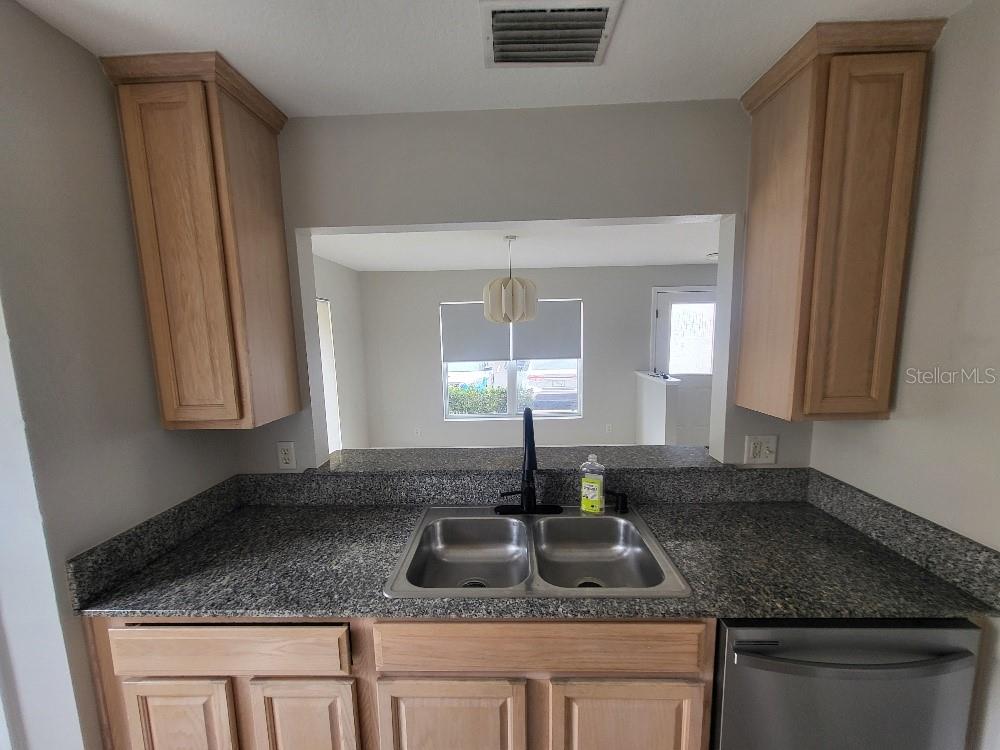 A kitchen sink area features granite countertops, light wood cabinets, and a pass-through window — 3874 MARINER DRIVE, ST PETERSBURG, FL