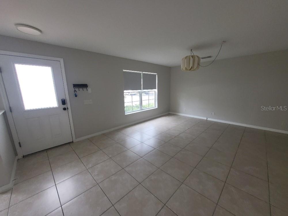 An empty room features light-colored tile flooring, a white front door, and a hanging light fixture — 3874 MARINER DRIVE, ST PETERSBURG, FL