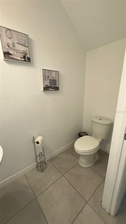 A small bathroom features a white toilet, tiled flooring, and two framed wall art pieces — 1457 DISCOVERY STREET, DAVENPORT, FL