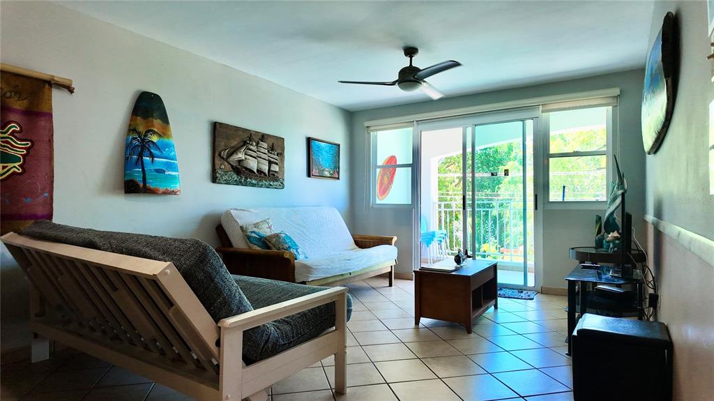 A living room features two futons, tile flooring, a ceiling fan, and sliding glass doors — 115 C.CAMBIJA UNIT 4B, RINCON, PR