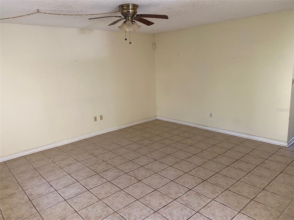 An empty room features light-colored walls, a ceiling fan, and beige tiled flooring — 11720 RAINTREE LAKE LANE UNIT B, TAMPA, FL