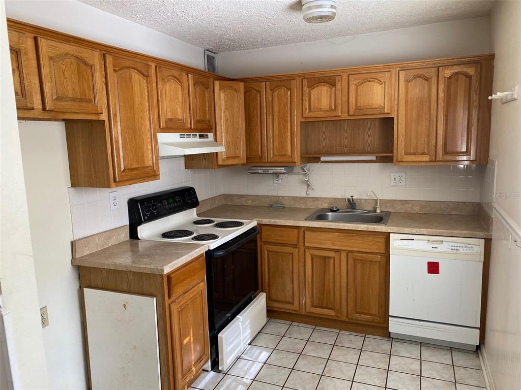 A kitchen features wood cabinets, laminate countertops, a white stove, and a white dishwasher — 11720 RAINTREE LAKE LANE UNIT B, TAMPA, FL