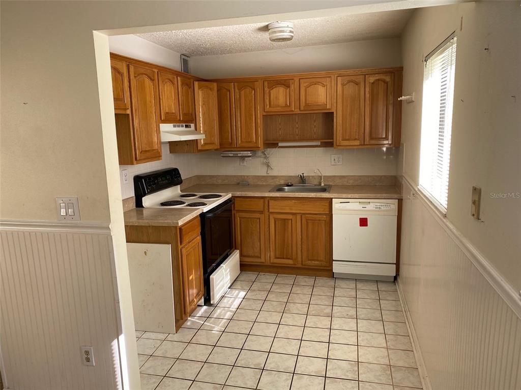 A kitchen with wood cabinets, white appliances, a tiled floor, and a window — 11720 RAINTREE LAKE LANE UNIT B, TAMPA, FL