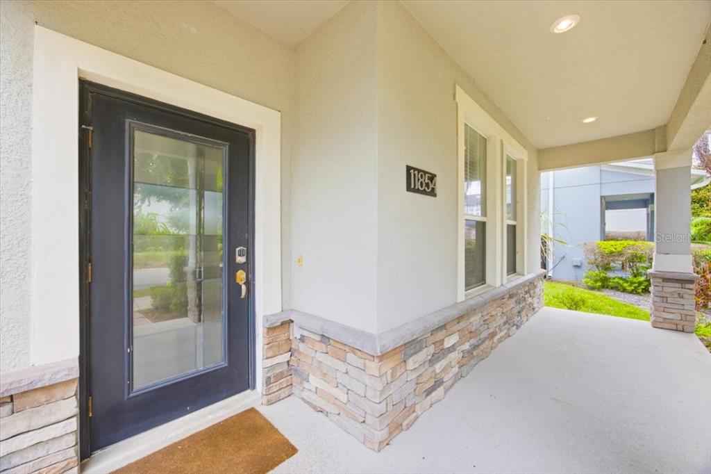 A covered front porch features a dark glass-paneled door and stone veneer siding — 11854 SONNET AVE, ORLANDO, FL