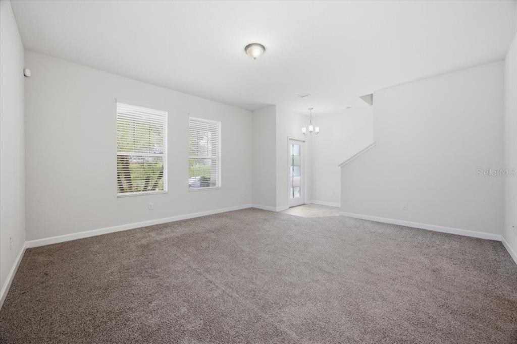 An empty room features gray carpeting, white walls, two windows, and a staircase — 11854 SONNET AVE, ORLANDO, FL