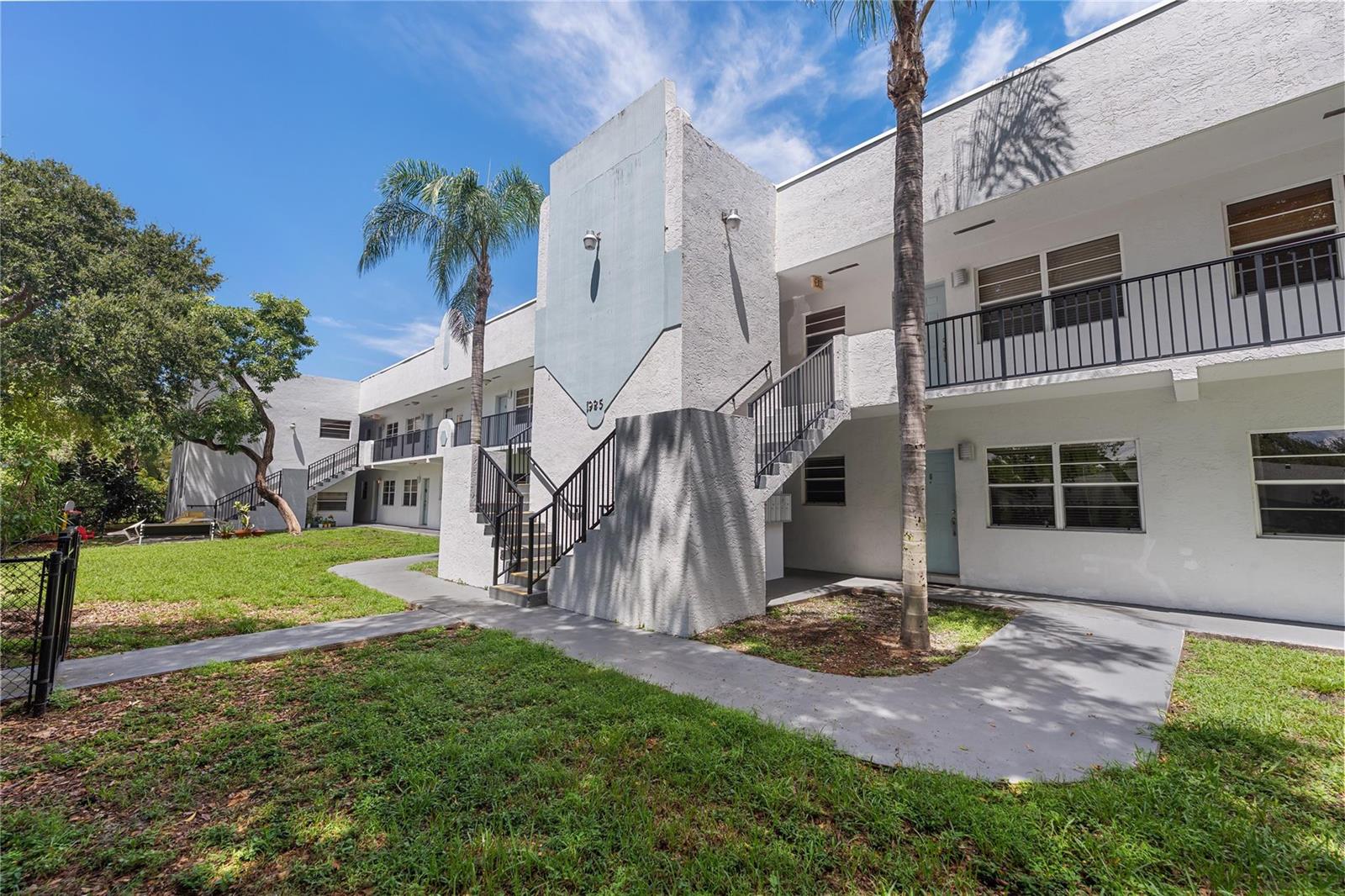 A two-story white apartment building features exterior staircases, balconies, and palm trees on the lawn — 1925 Madison Street # 14, Hollywood FL 33020, HOLLYWOOD, FL