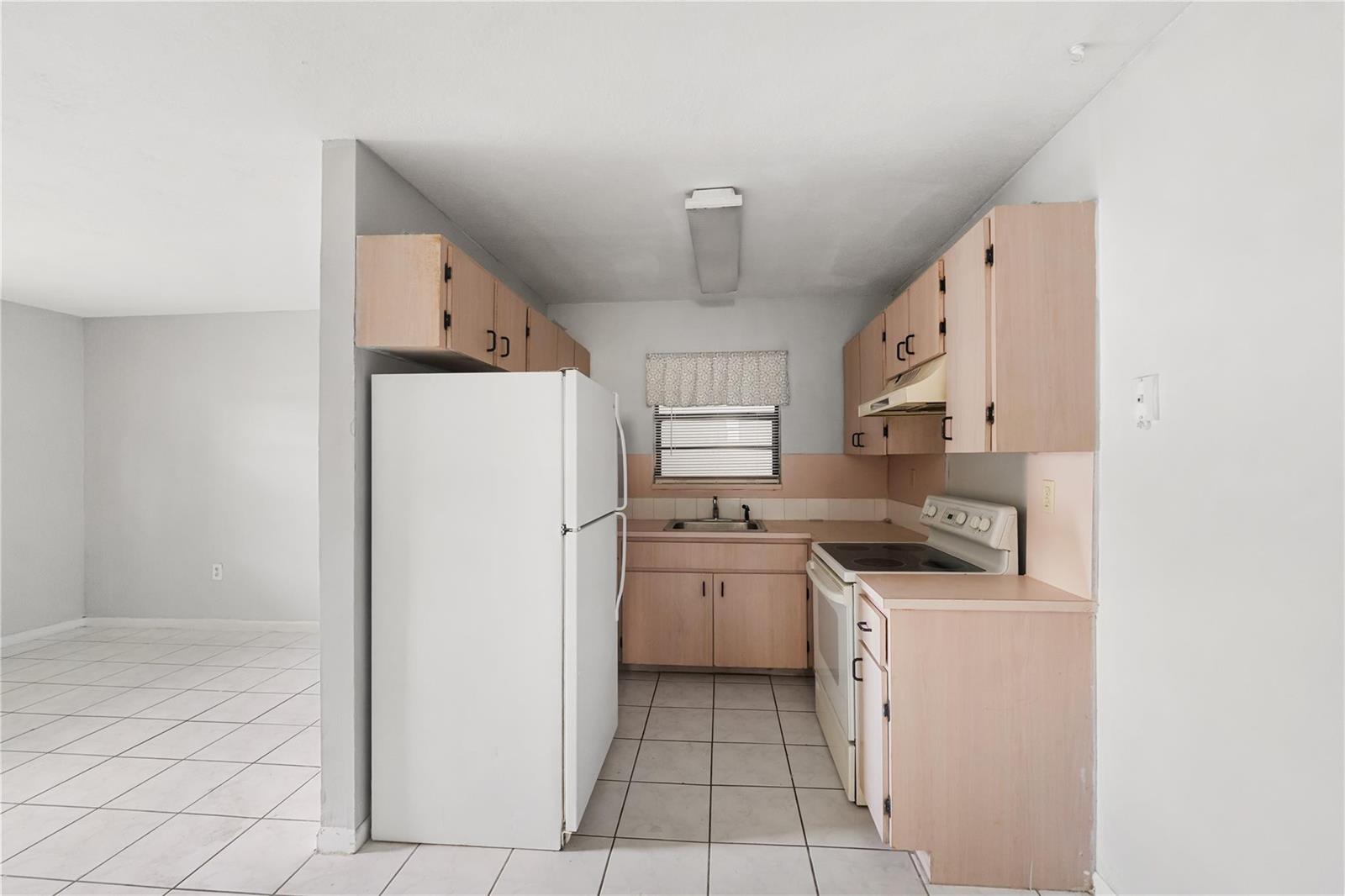 A galley kitchen features light wood cabinets, white appliances, and white tile flooring — 1925 Madison Street # 14, Hollywood FL 33020, HOLLYWOOD, FL