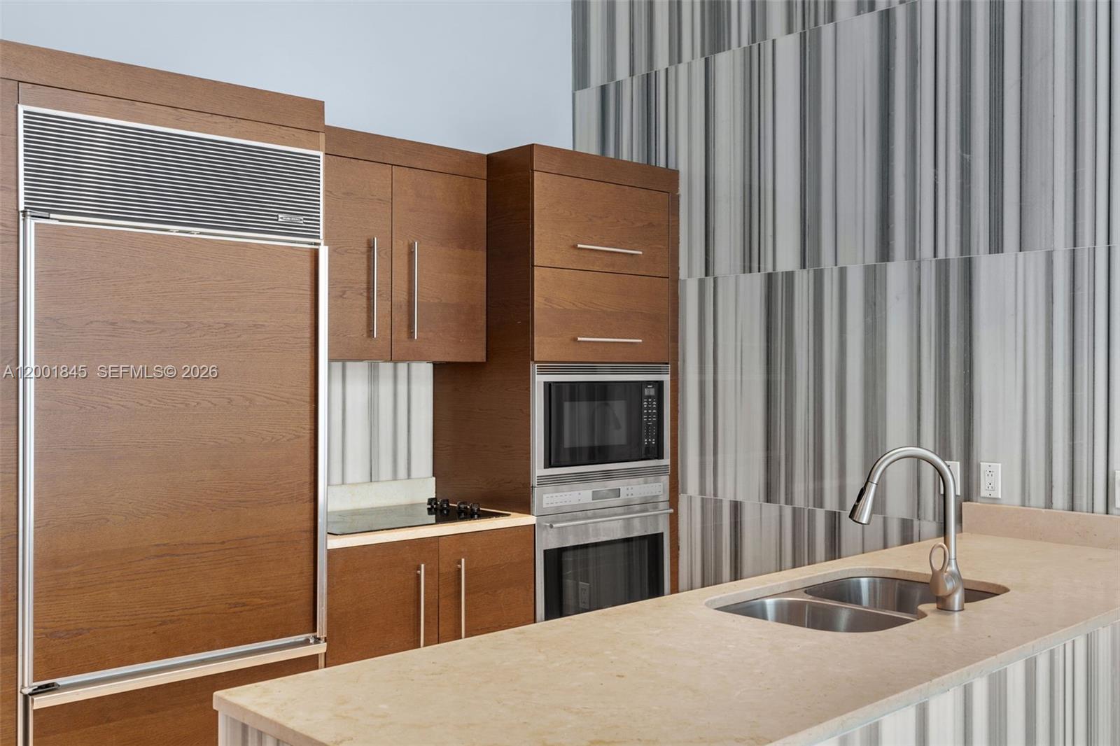 A modern kitchen features wood-paneled cabinetry, stainless steel appliances, and a light stone countertop — 475 Brickell Ave # 2812, Miami FL 33131, MIAMI, FL