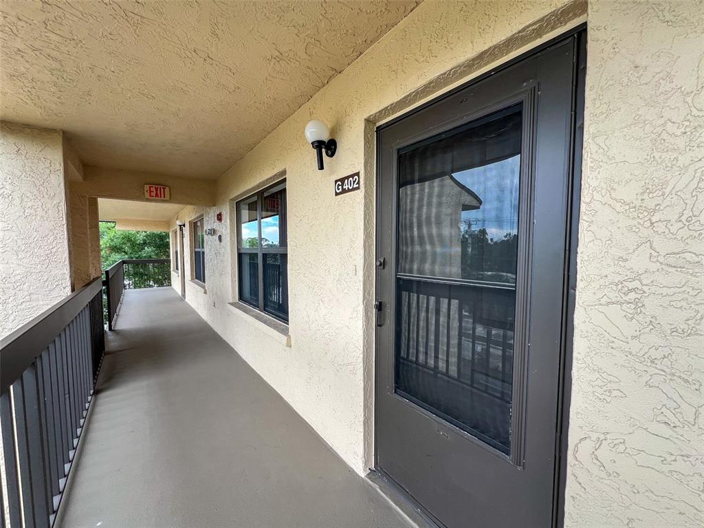 An exterior walkway leads to a dark-framed door marked G402 on a stucco building — 625 30TH AVENUE W UNIT G402, BRADENTON, FL