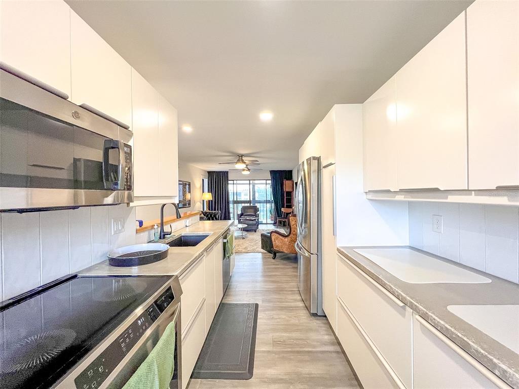 A galley kitchen features white flat-panel cabinets, stainless steel appliances, and light wood-look flooring — 625 30TH AVENUE W UNIT G402, BRADENTON, FL