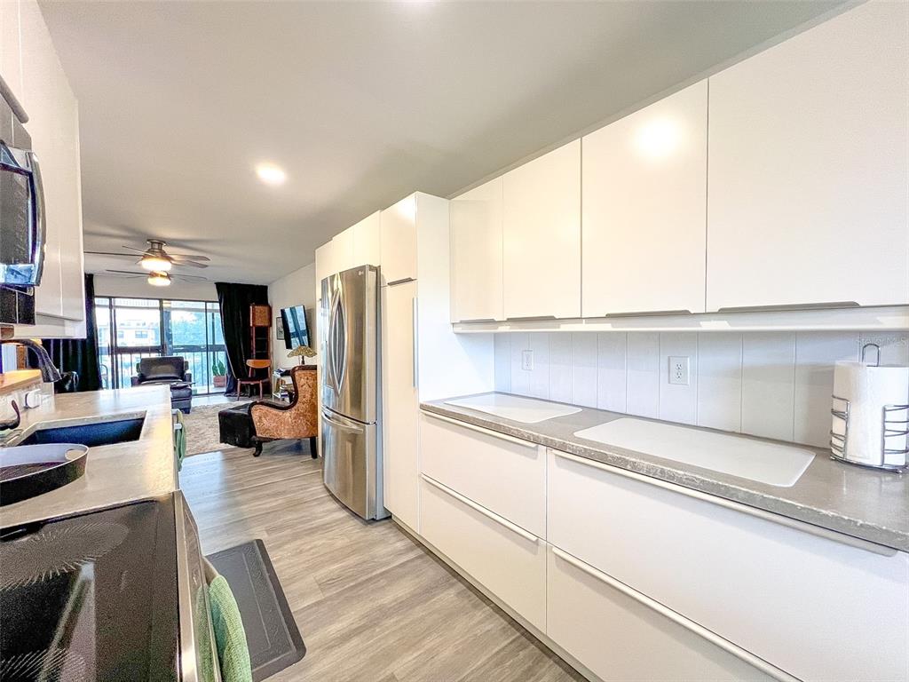 A modern kitchen features white flat-panel cabinetry, stainless steel appliances, and light wood-look flooring — 625 30TH AVENUE W UNIT G402, BRADENTON, FL