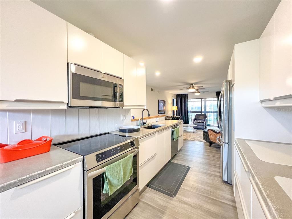 A modern galley kitchen features white cabinets, stainless steel appliances, and light wood-look flooring — 625 30TH AVENUE W UNIT G402, BRADENTON, FL