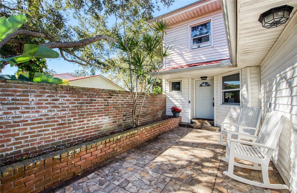 A patio with a brick wall, tiled floor, and two white rocking chairs by a house — 1423 WATER VIEW DRIVE W, LARGO, FL
