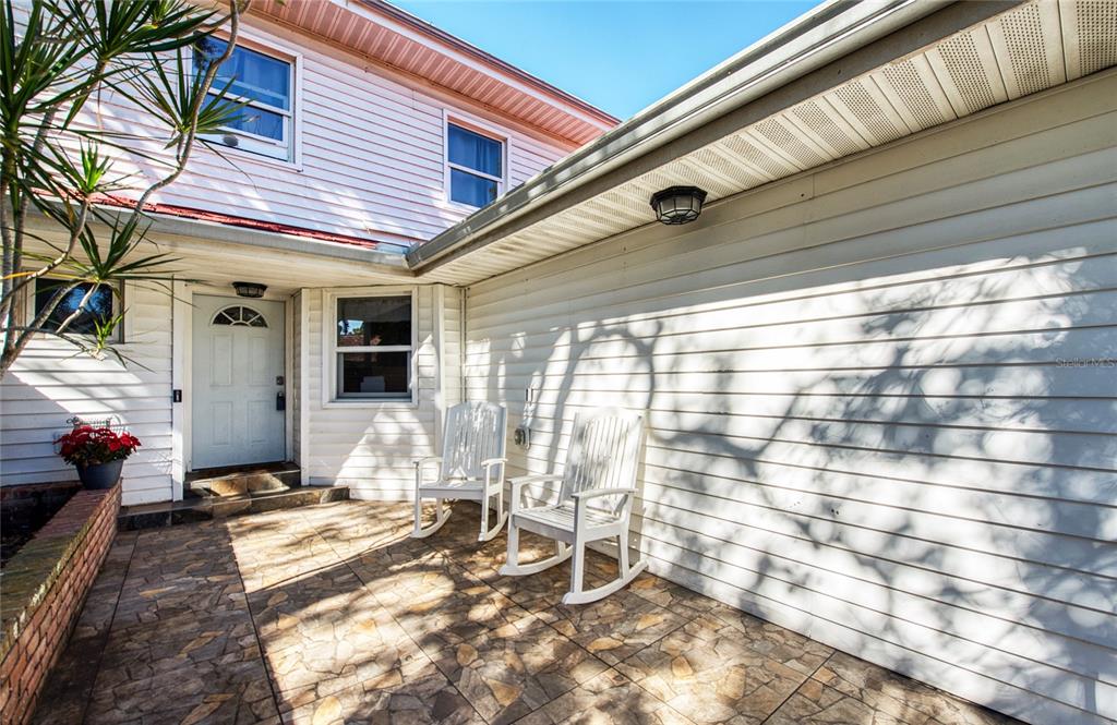 A paved patio area features two white rocking chairs in front of a house exterior — 1423 WATER VIEW DRIVE W, LARGO, FL