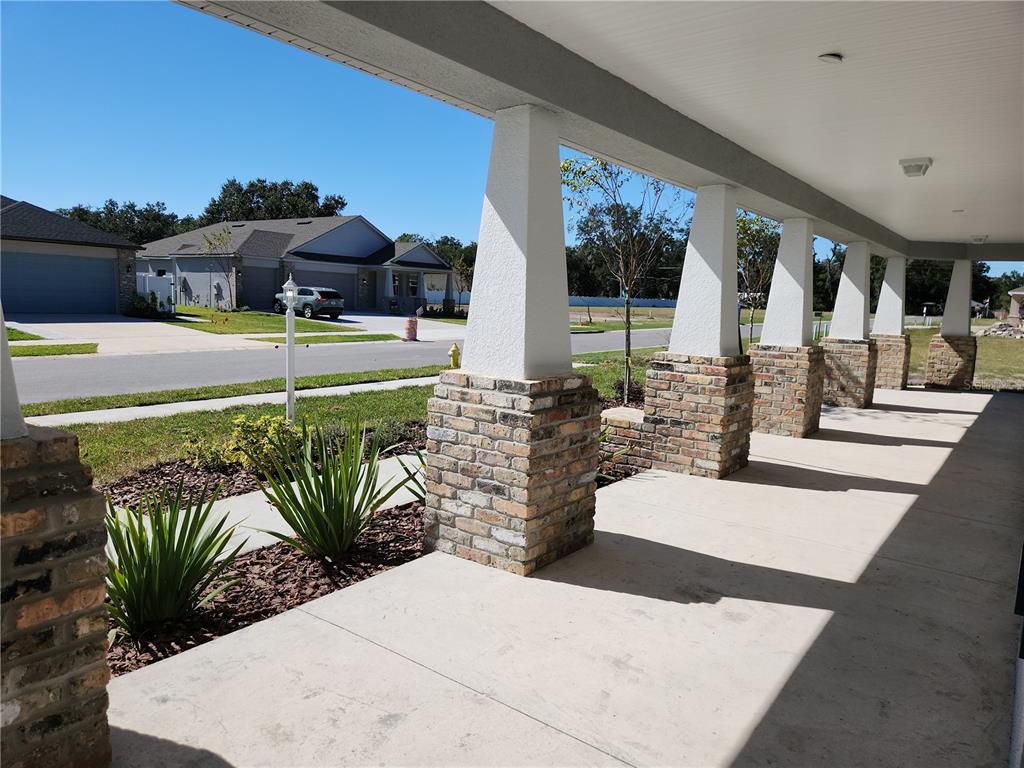 A covered porch features concrete flooring and white tapered columns set on brick bases — 416 SHANNON ESTATES COURT, PLANT CITY, FL