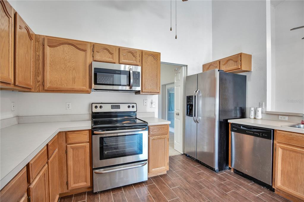 A kitchen features wood cabinets, stainless steel appliances, white countertops, and wood-look tile flooring — 6019 LONG PEAK DRIVE, ORLANDO, FL