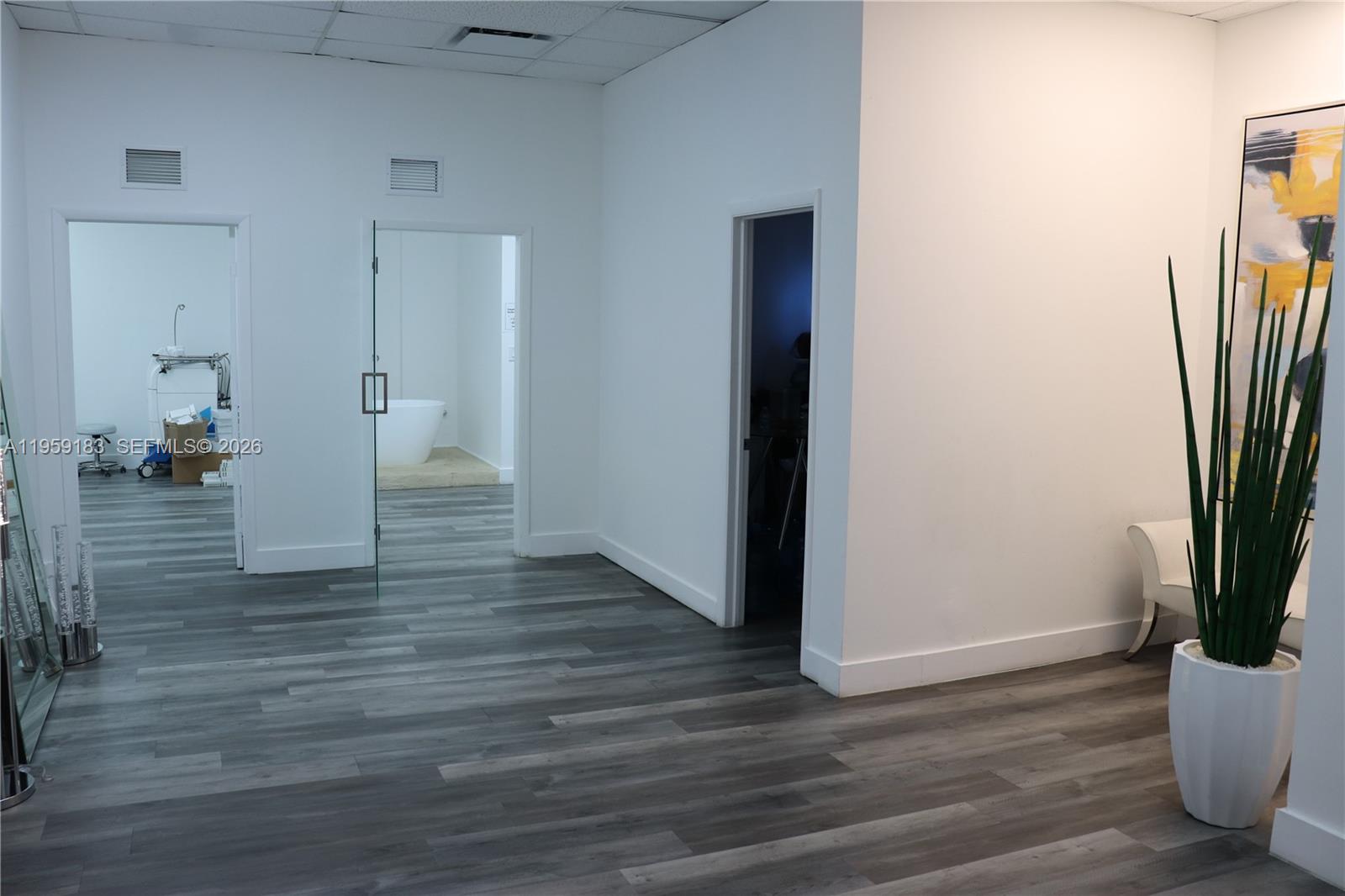 A bright, minimalist office space features gray wood-look flooring, white walls, and three doorways — 3724-3728 Davie Rd, Davie FL 33314, DAVIE, FL
