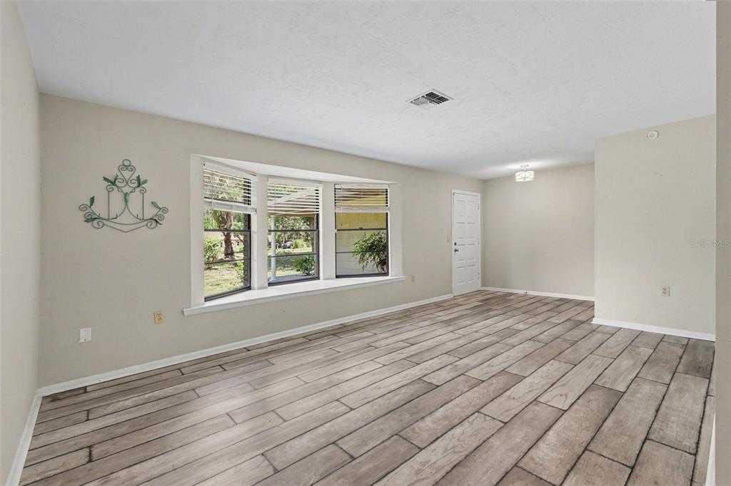 An empty living room features light-colored walls, wood-look tile flooring, and a large bay window — 9491 SW 200TH COURT, DUNNELLON, FL