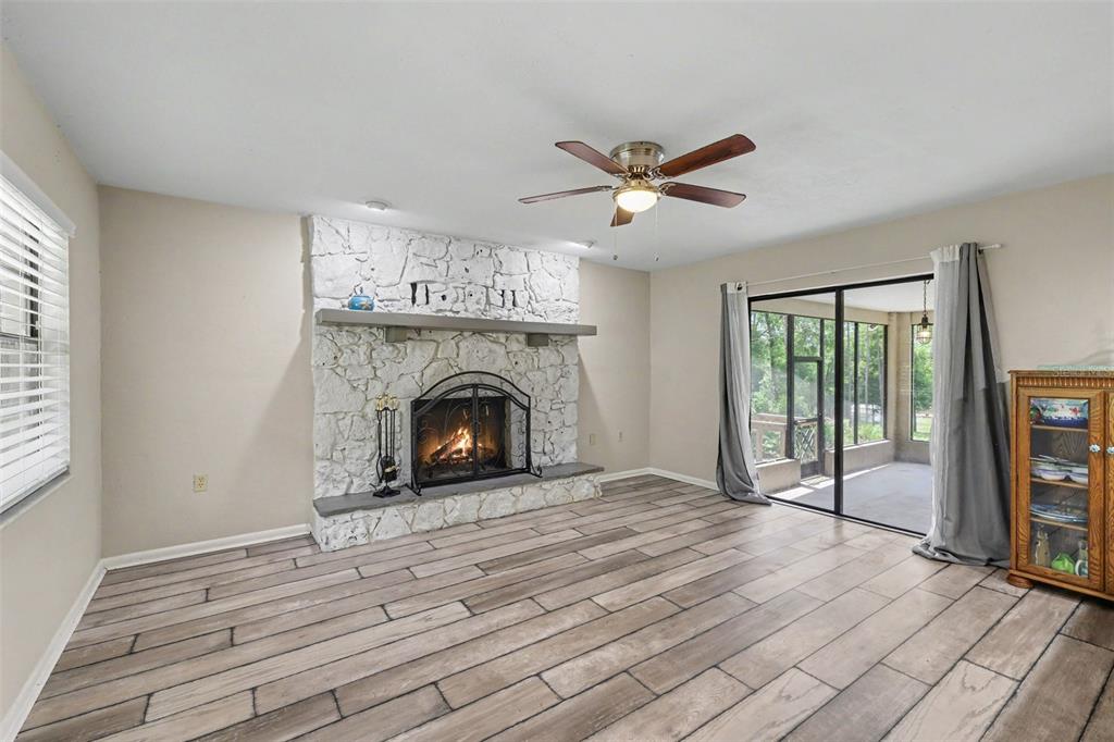 A living room features a white stone fireplace, wood-look tile flooring, and a sliding glass door — 9491 SW 200TH COURT, DUNNELLON, FL