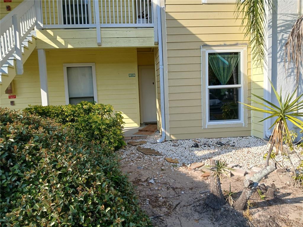 A yellow two-story apartment building exterior features a ground-level entrance, windows, and landscaping — 455 ALT 19 S UNIT 121, PALM HARBOR, FL