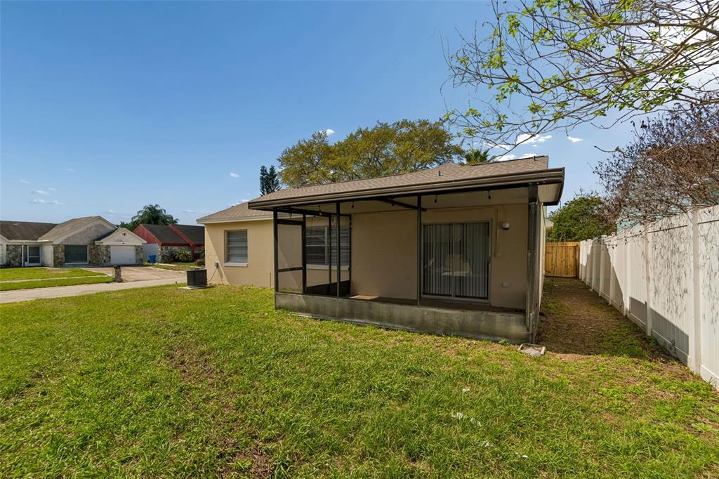 A backyard view of a house with a screened-in porch and a white vinyl fence — 8301 IBERIA PLACE, TAMPA, FL