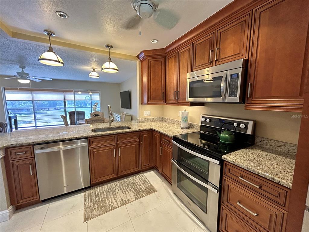 A kitchen features wood cabinets, granite countertops, stainless steel appliances, and tile flooring — 4040 IRONWOOD CIRCLE UNIT 404F, BRADENTON, FL