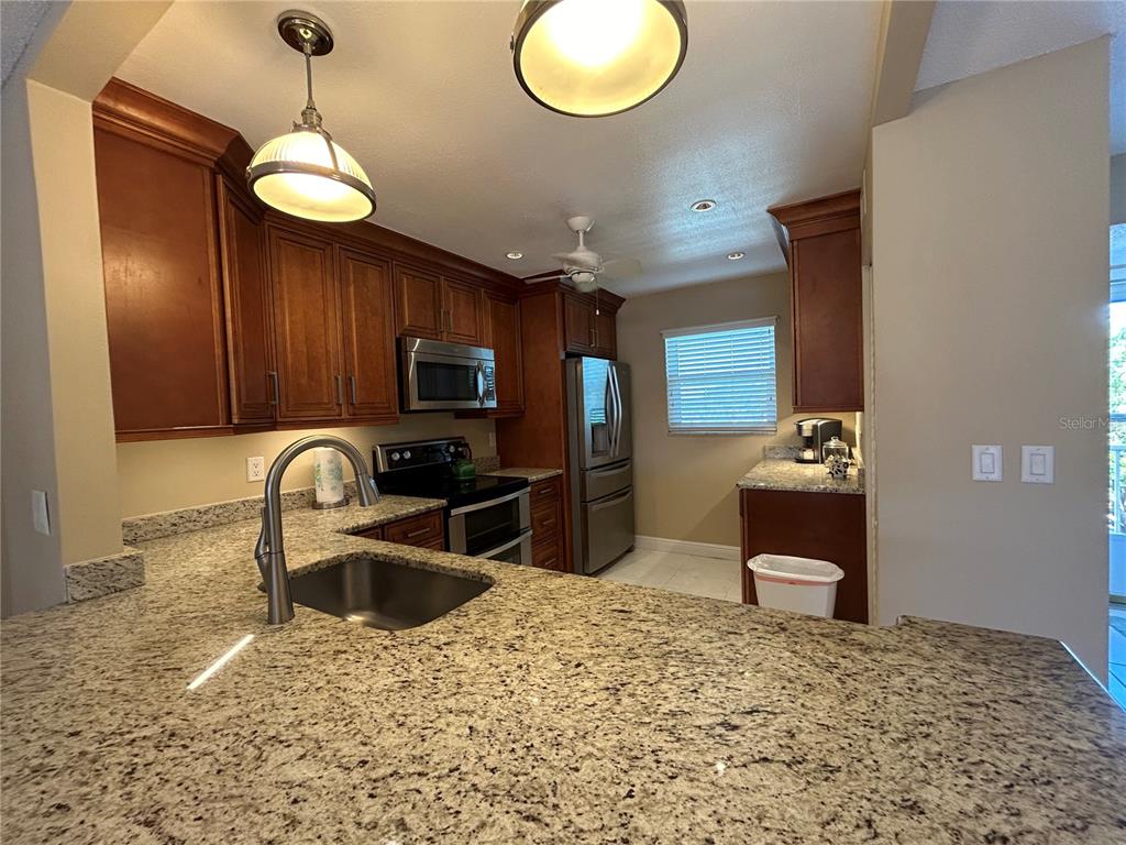 A kitchen features granite countertops, wood cabinets, stainless steel appliances, and a pendant light — 4040 IRONWOOD CIRCLE UNIT 404F, BRADENTON, FL