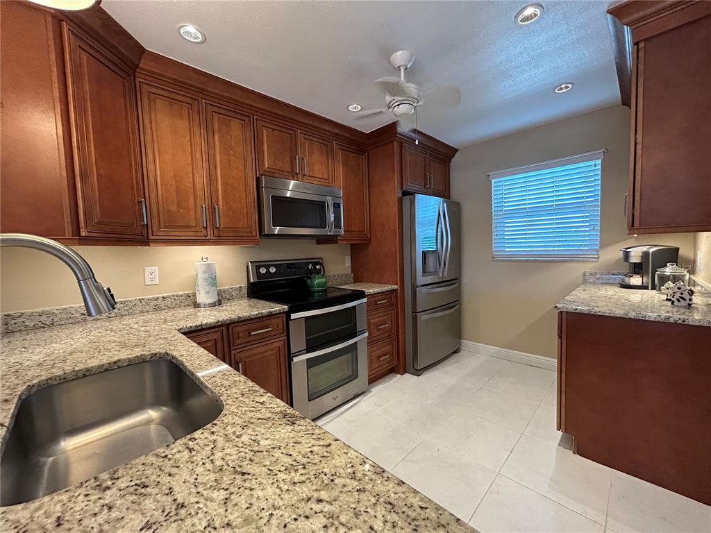 A kitchen features wood cabinets, granite countertops, stainless steel appliances, and light-colored tile flooring — 4040 IRONWOOD CIRCLE UNIT 404F, BRADENTON, FL