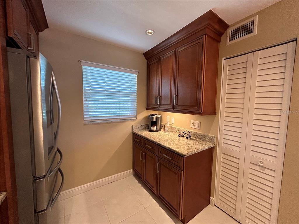 A kitchen area features dark wood cabinets, granite countertops, a stainless refrigerator, and louvered doors — 4040 IRONWOOD CIRCLE UNIT 404F, BRADENTON, FL