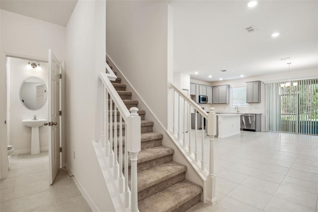 A carpeted staircase sits between a small bathroom and an open-concept kitchen and living area — 5756 SPOTTED HARRIER WAY, LITHIA, FL