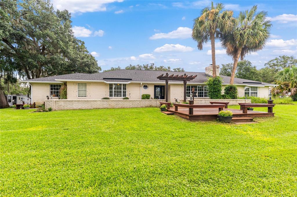 A single-story brick house features a wooden deck and pergola in a large grassy yard — 11851 SW 38TH STREET, OCALA, FL
