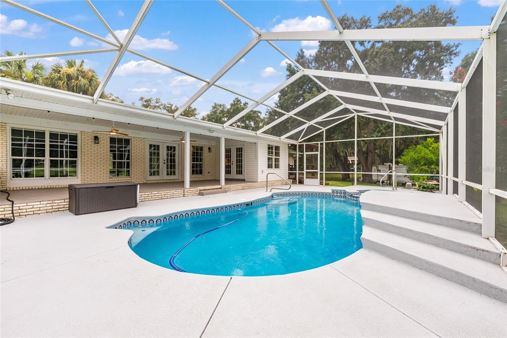A screened-in patio features a swimming pool with steps and a brick-walled house exterior — 11851 SW 38TH STREET, OCALA, FL
