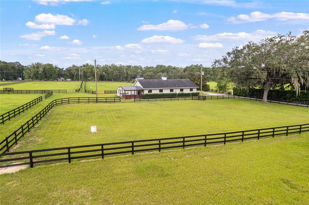 A white barn with a dark roof sits in a fenced pasture under a blue sky — 11851 SW 38TH STREET, OCALA, FL
