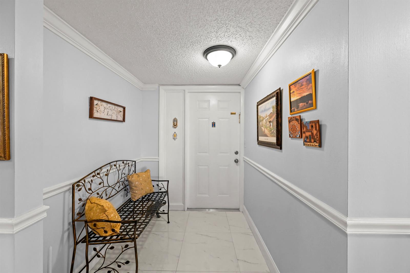 An entryway features a metal bench, light-colored tile flooring, and several wall decorations — 750 Egret Circle # 6509, Delray Beach FL 33444, DELRAY BEACH, FL