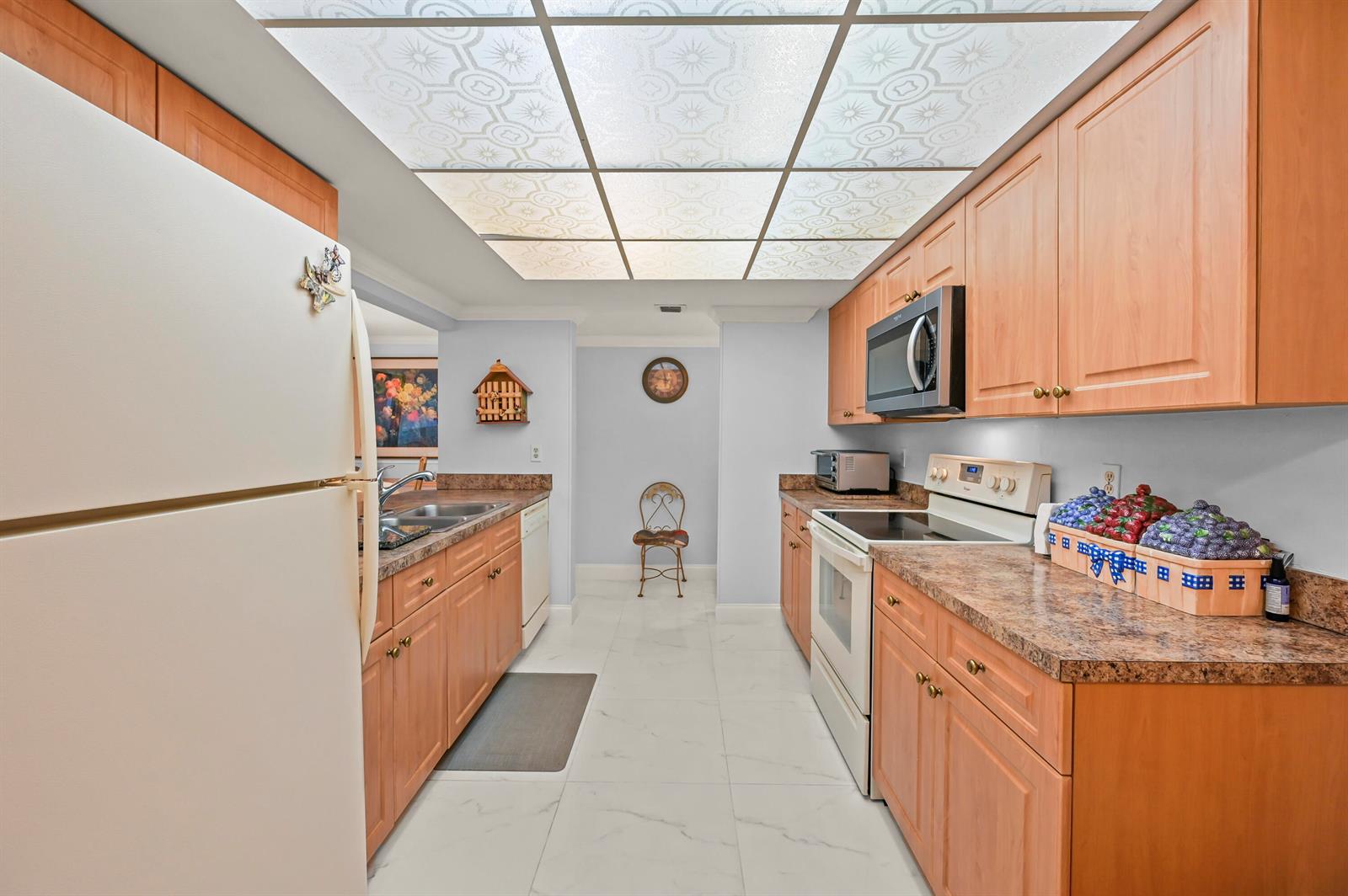 A galley kitchen features light wood cabinets, laminate countertops, white appliances, and a drop ceiling — 750 Egret Circle # 6509, Delray Beach FL 33444, DELRAY BEACH, FL