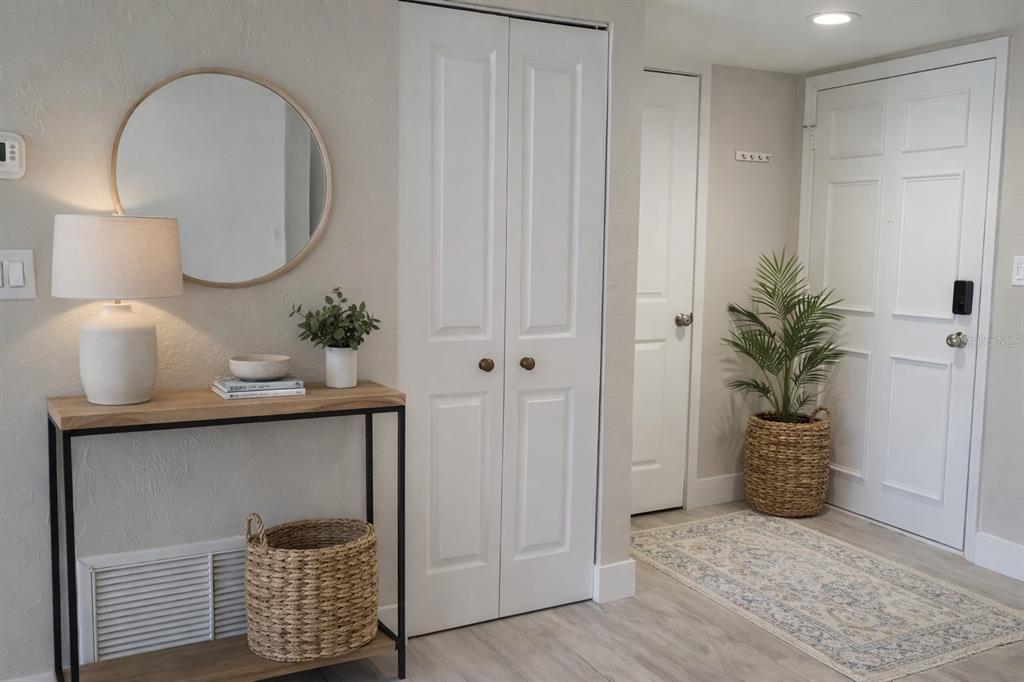 A bright entryway features a console table, a round mirror, and a white closet door — 500 TREASURE ISLAND CAUSEWAY UNIT 106, TREASURE ISLAND, FL