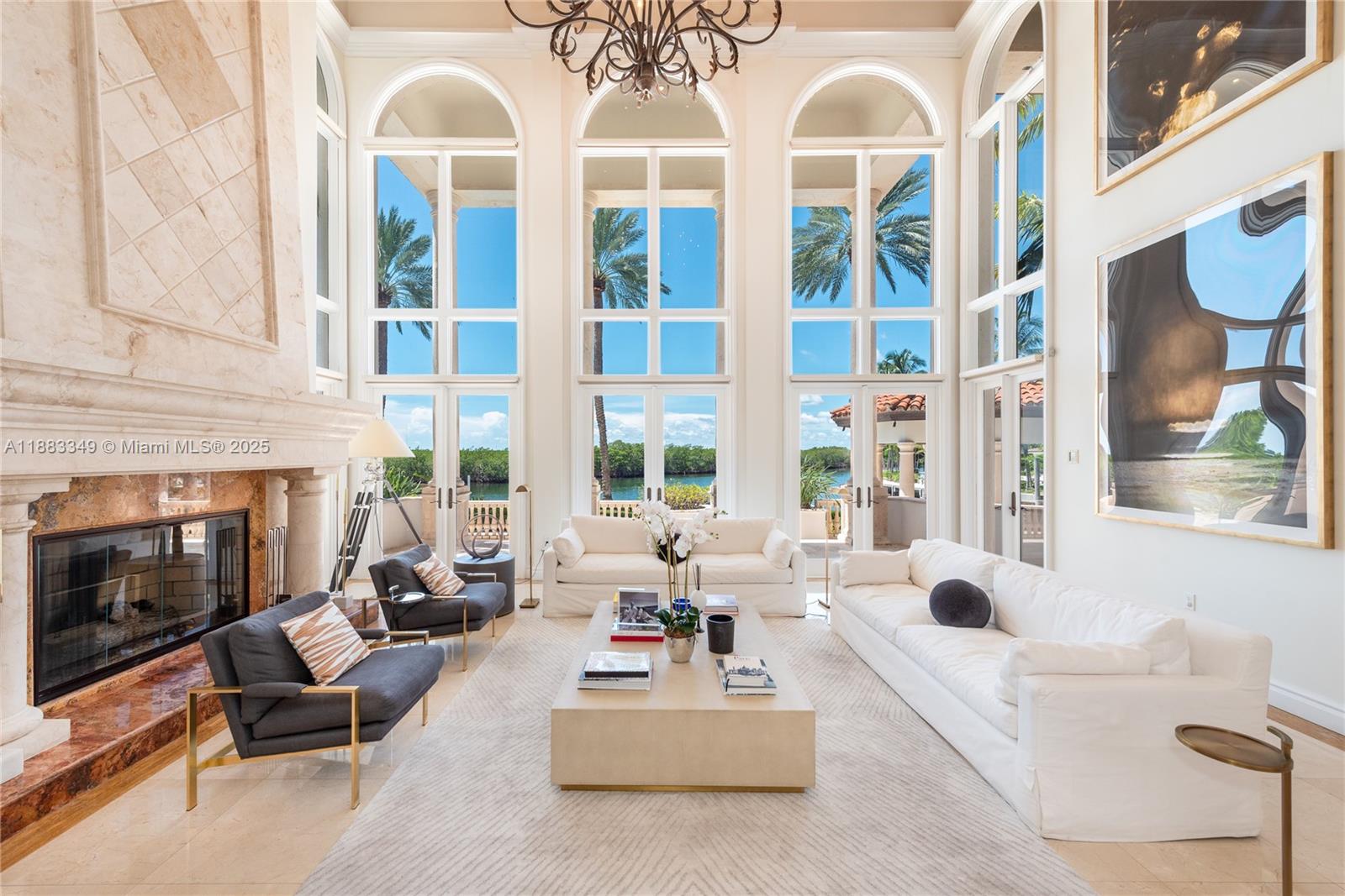 A bright living room features a tall stone fireplace, floor-to-ceiling windows, and waterfront views — 260 Cape Florida Dr, Key Biscayne FL 33149, KEY BISCAYNE, FL