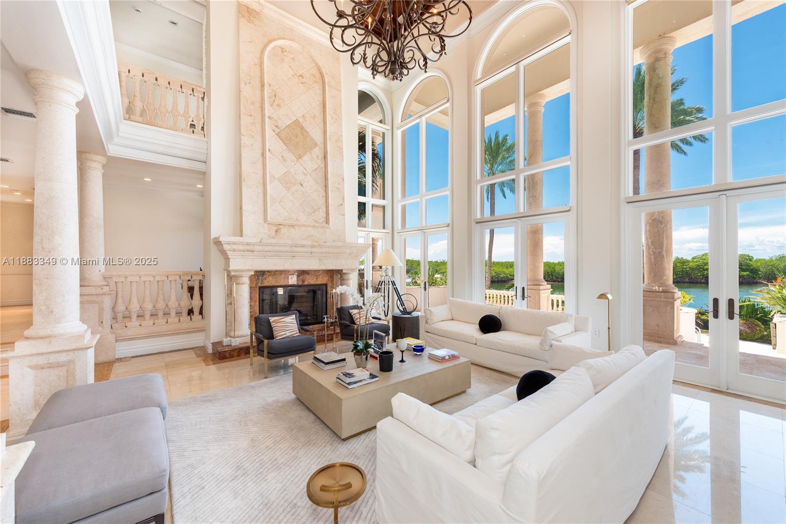 A spacious living room features a tall stone fireplace, floor-to-ceiling windows, and outdoor water views — 260 Cape Florida Dr, Key Biscayne FL 33149, KEY BISCAYNE, FL