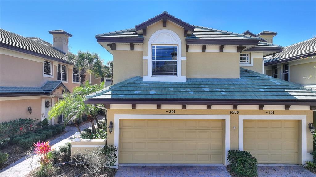 A two-story stucco building features a two-car garage and a green tiled roof — 6508 MOORINGS POINT CIRCLE UNIT 201, LAKEWOOD RANCH, FL
