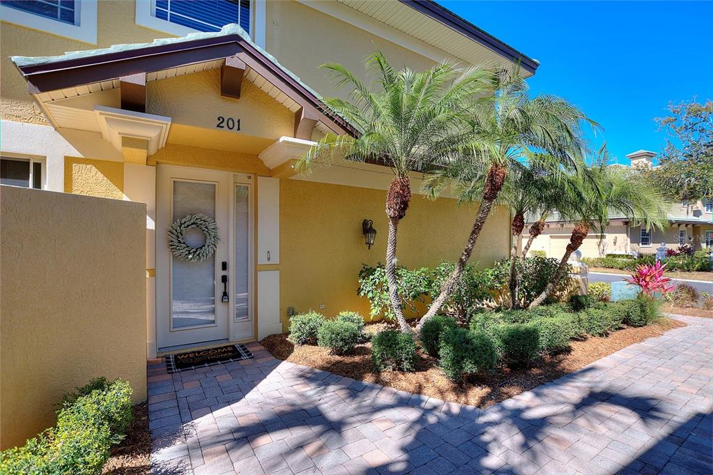 The exterior of a yellow house features a front door with a wreath and palm trees — 6508 MOORINGS POINT CIRCLE UNIT 201, LAKEWOOD RANCH, FL