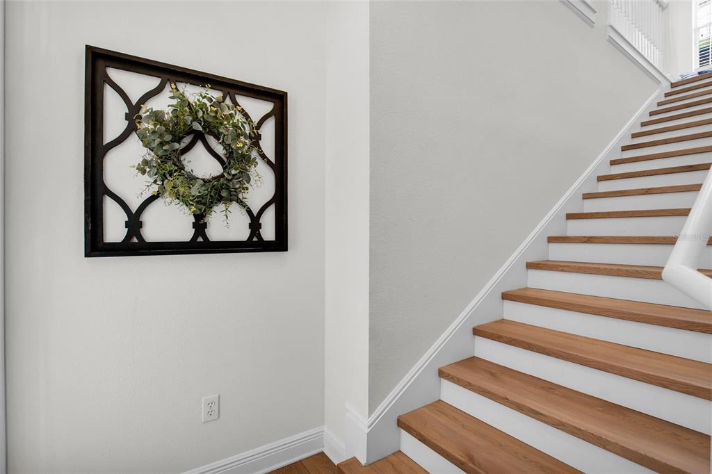 A staircase with wooden treads and white risers sits beside a wall with a wreath — 6508 MOORINGS POINT CIRCLE UNIT 201, LAKEWOOD RANCH, FL