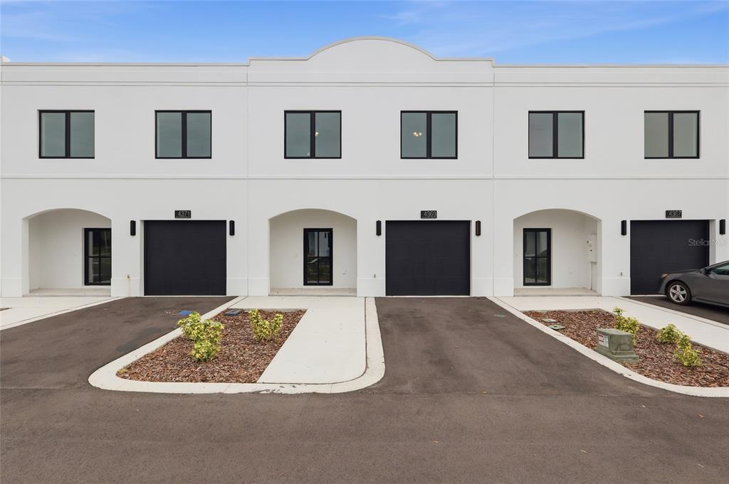 A row of three modern white townhomes with black garage doors and paved driveways — 4369 CAMBIO GARDENS COURT, TAMPA, FL