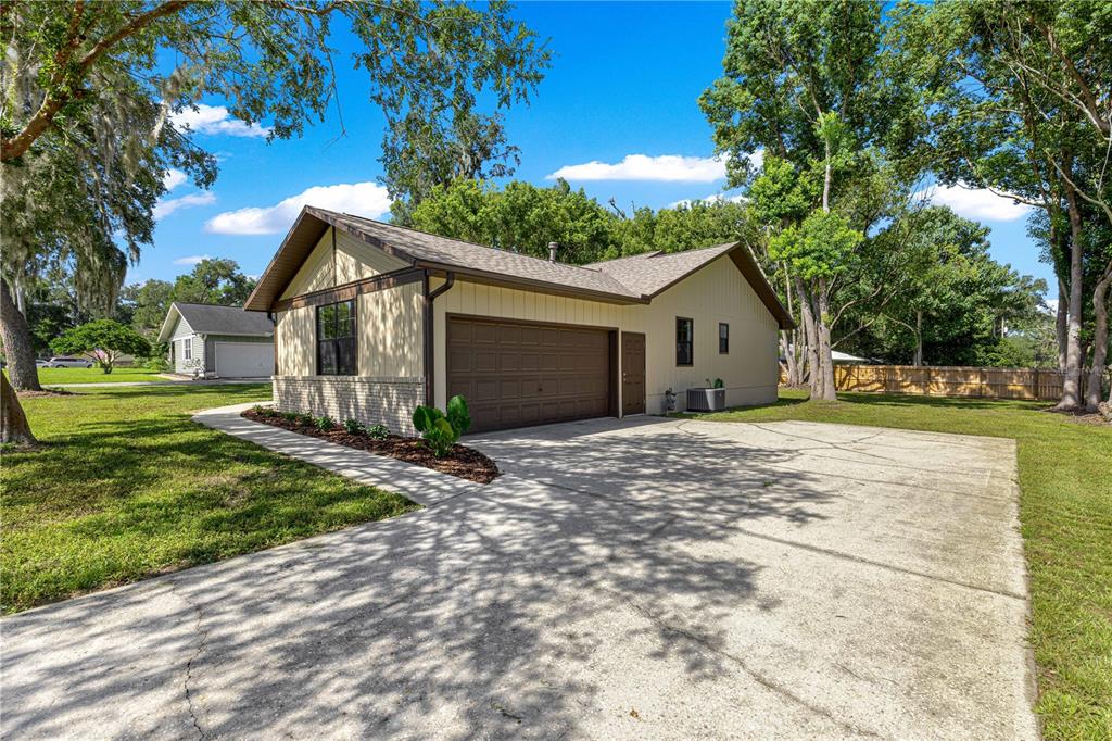 A tan house with a brown garage door, concrete driveway, and surrounding trees under blue skies — 804 NE 46TH COURT, OCALA, FL