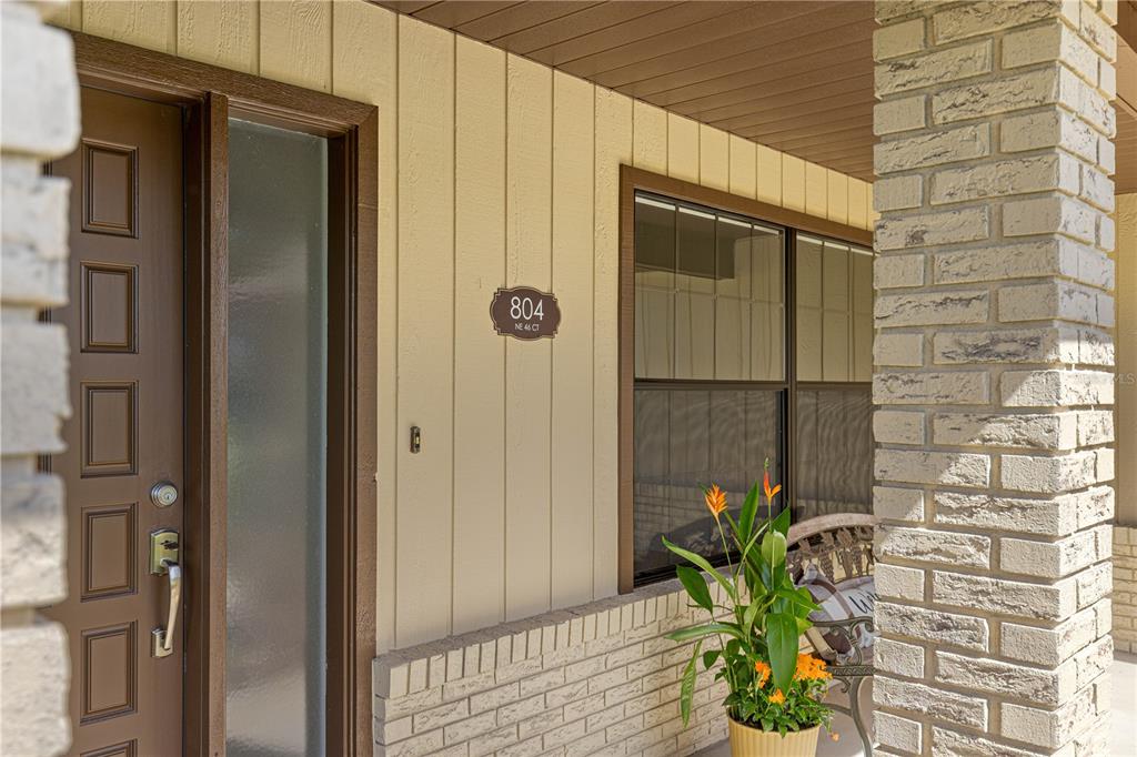 A front entryway features a brown door, vertical siding, a brick pillar, and a potted plant — 804 NE 46TH COURT, OCALA, FL
