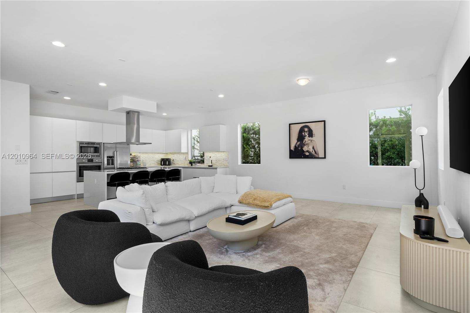 A modern open-concept living room features a white sectional, black armchairs, and a kitchen island — 9915 NW 75th St # 9915, Doral FL 33178, DORAL, FL